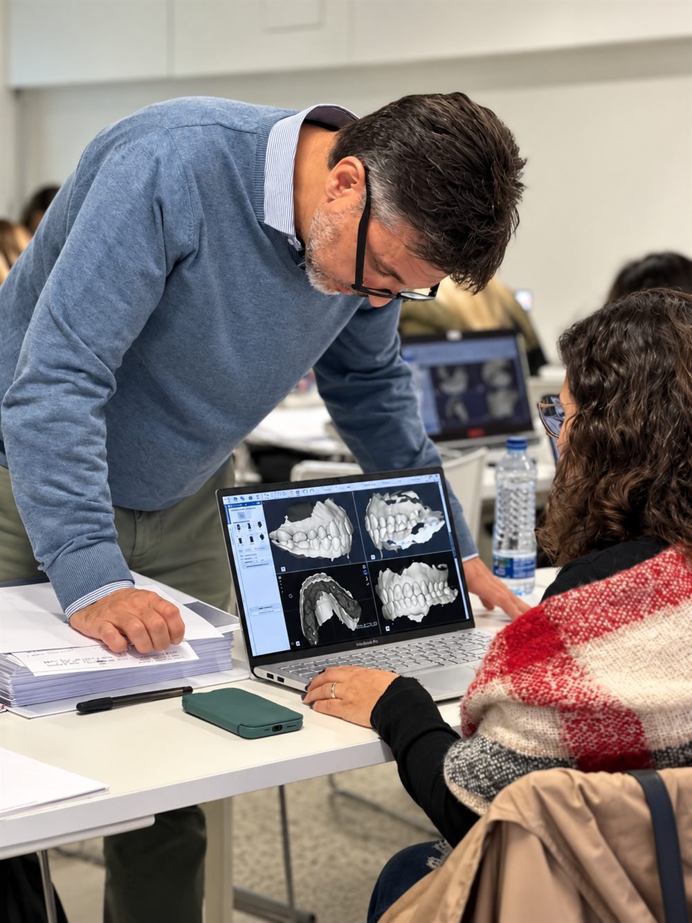 Docente revisando una planificación 3D de arcadas dentales junto a una participante